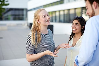 Drei diskutierende Studierende vor der Uni