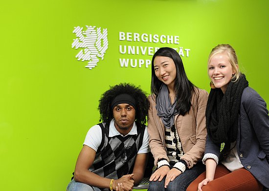 Drei Studierende vor Uni Logo der Uni Wuppertal