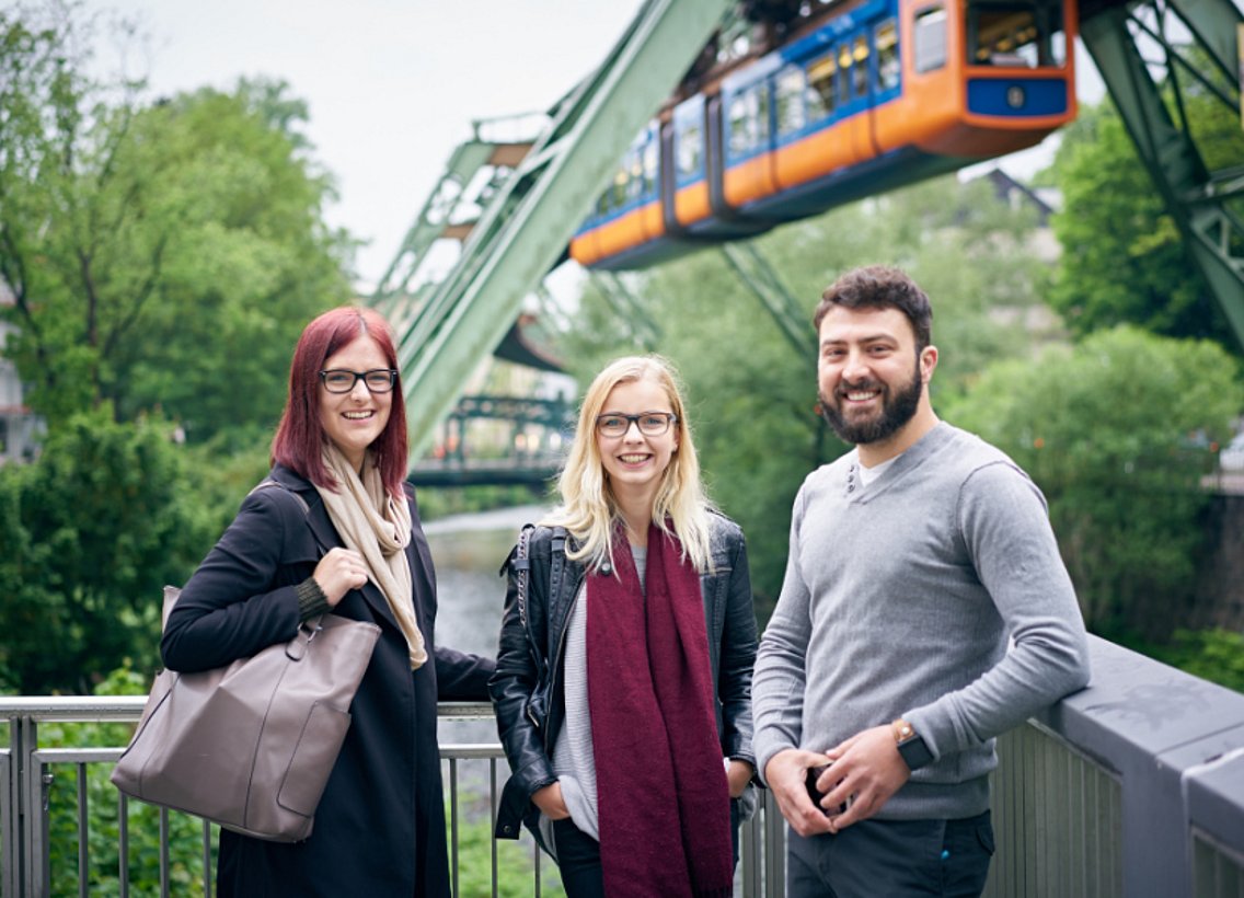 Drei Studierende, im Hintergrund die Schwebebahn